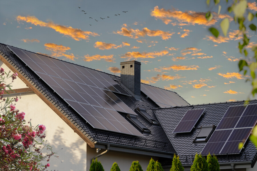 Hausdach mit Solarmodulen und Sonnenuntergang im Hintergrund.