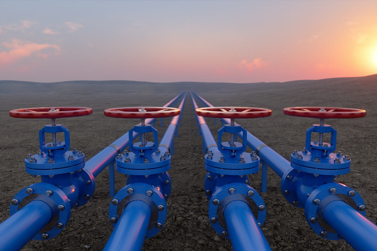 Blaue Gaspipelines in steiniger Landschaft und Sonnenuntergang am Horizont.