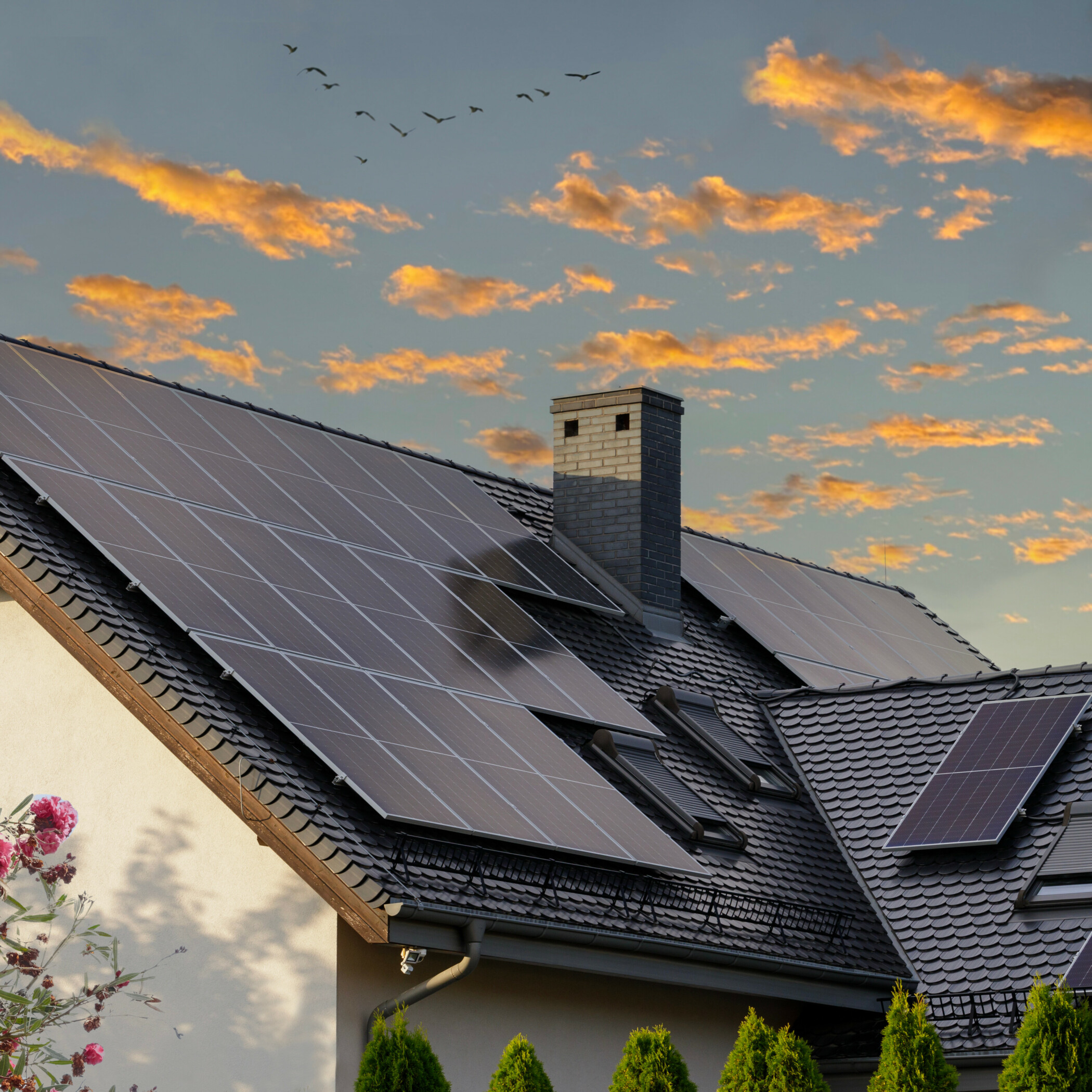 Hausdach mit Solarmodulen und Sonnenuntergang im Hintergrund.