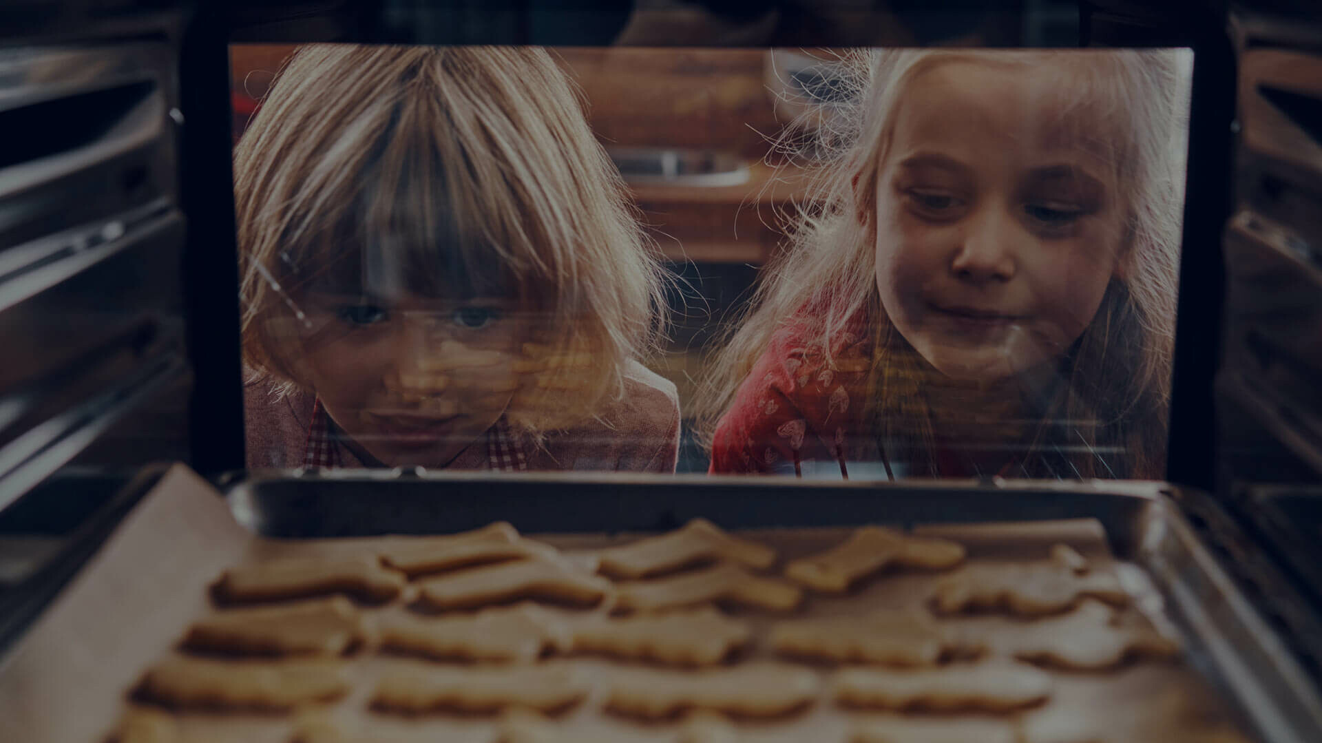 Zwei Kinder schauen in den Backofen, in dem Plätzchen backen.