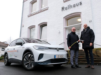 Bürgermeister von Much Norbert Büscher und rhenag-Vorstand Till-Cremer stehen vor dem Rathaus in Much neben einem rhenag eCarsharing-Auto und eröffnen das neue eCarsharing in Much.