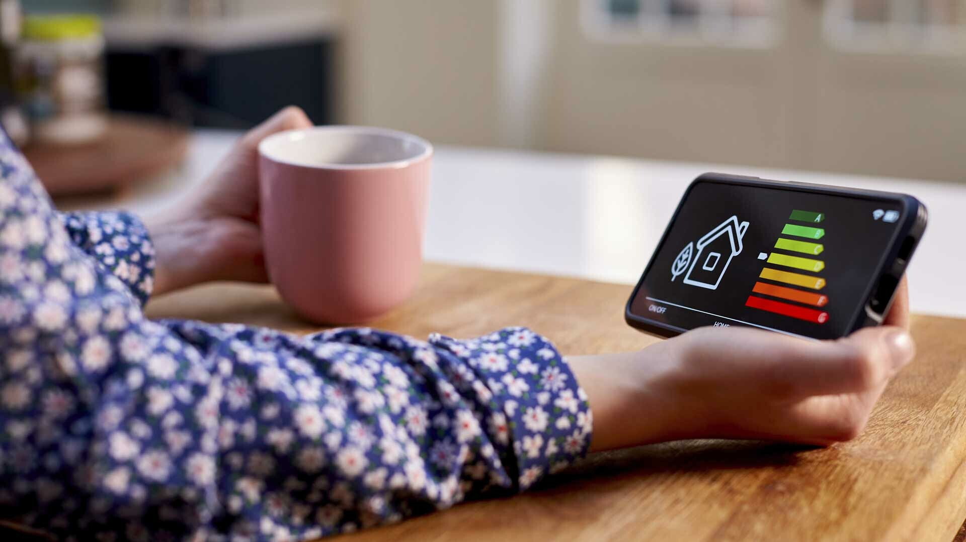 Energieeffizienzbild auf einem Mobiltelefon, Hand mit Kaffeetasse