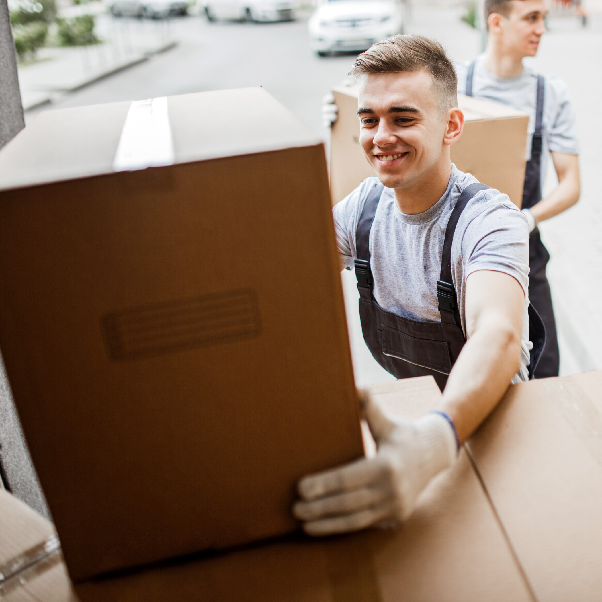 Lächelndes junges Paar mit dunklen Haaren steht vor einem gelben Hintergrund und schaut sich etwas auf einem Laptop an.