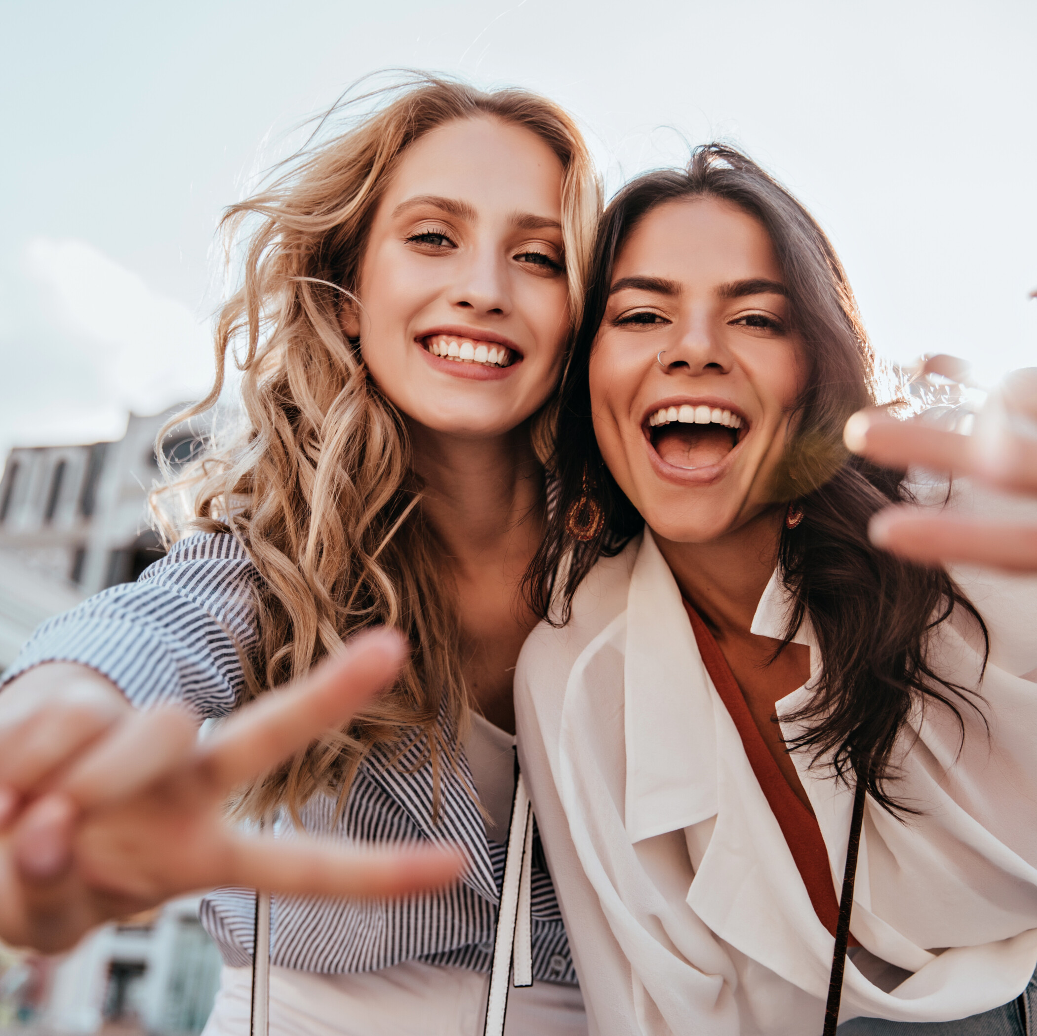 Frau und Mann mit dunklen Haaren im Hintergrund formen mit jeweils einer Hand ein gemeinsames Herz, welches im Vordergrund steht.