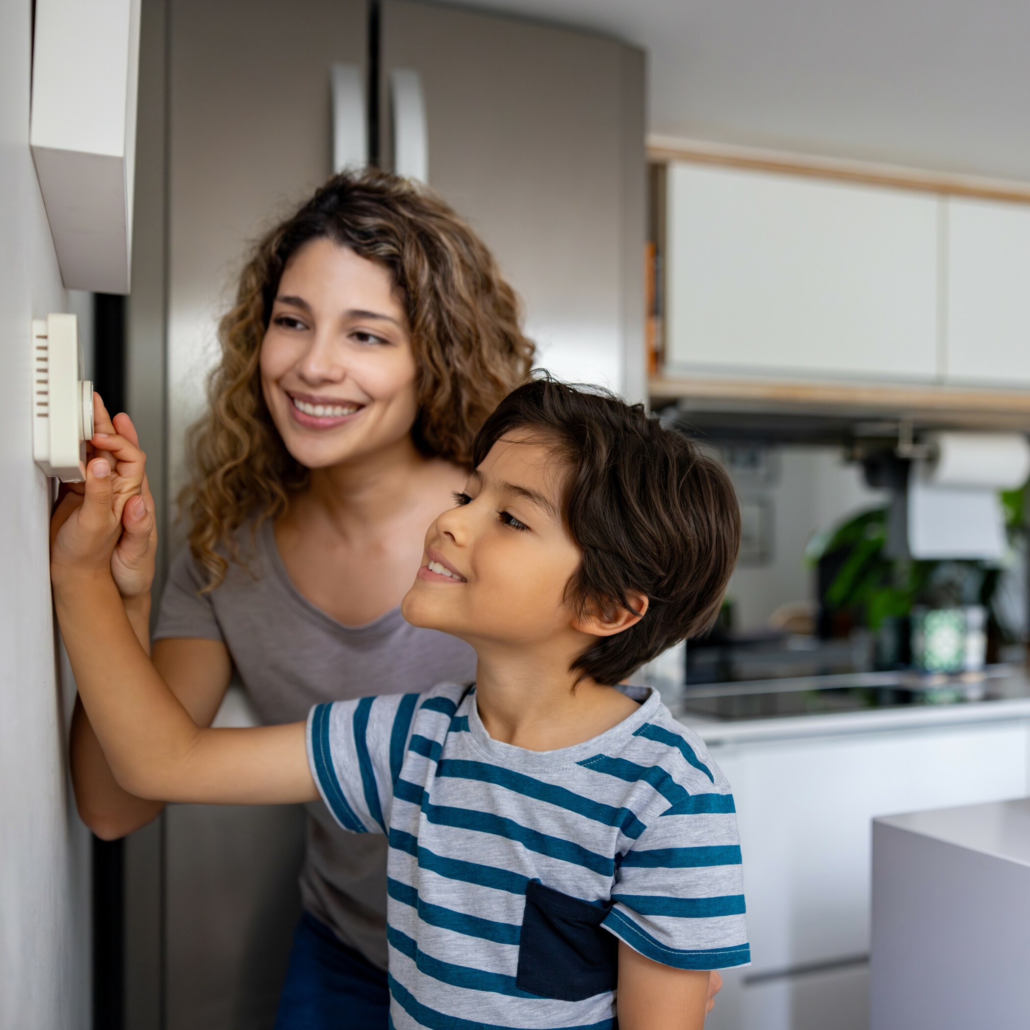 Mutter schaut zu, wie ihr Kind die Temperatur am Thermostat in der Küche einstellt.