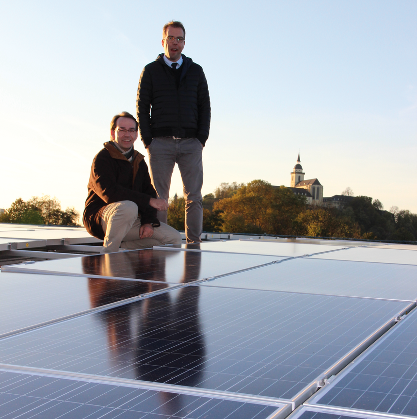 Zwei rhenag-Mitarbeiter stehen auf dem Dach des rhenag-Dienstleistungszentrums in der Wilhelm-Ostwald-Straße. Das Dach ist belegt mit Photovoltaikmodulen.