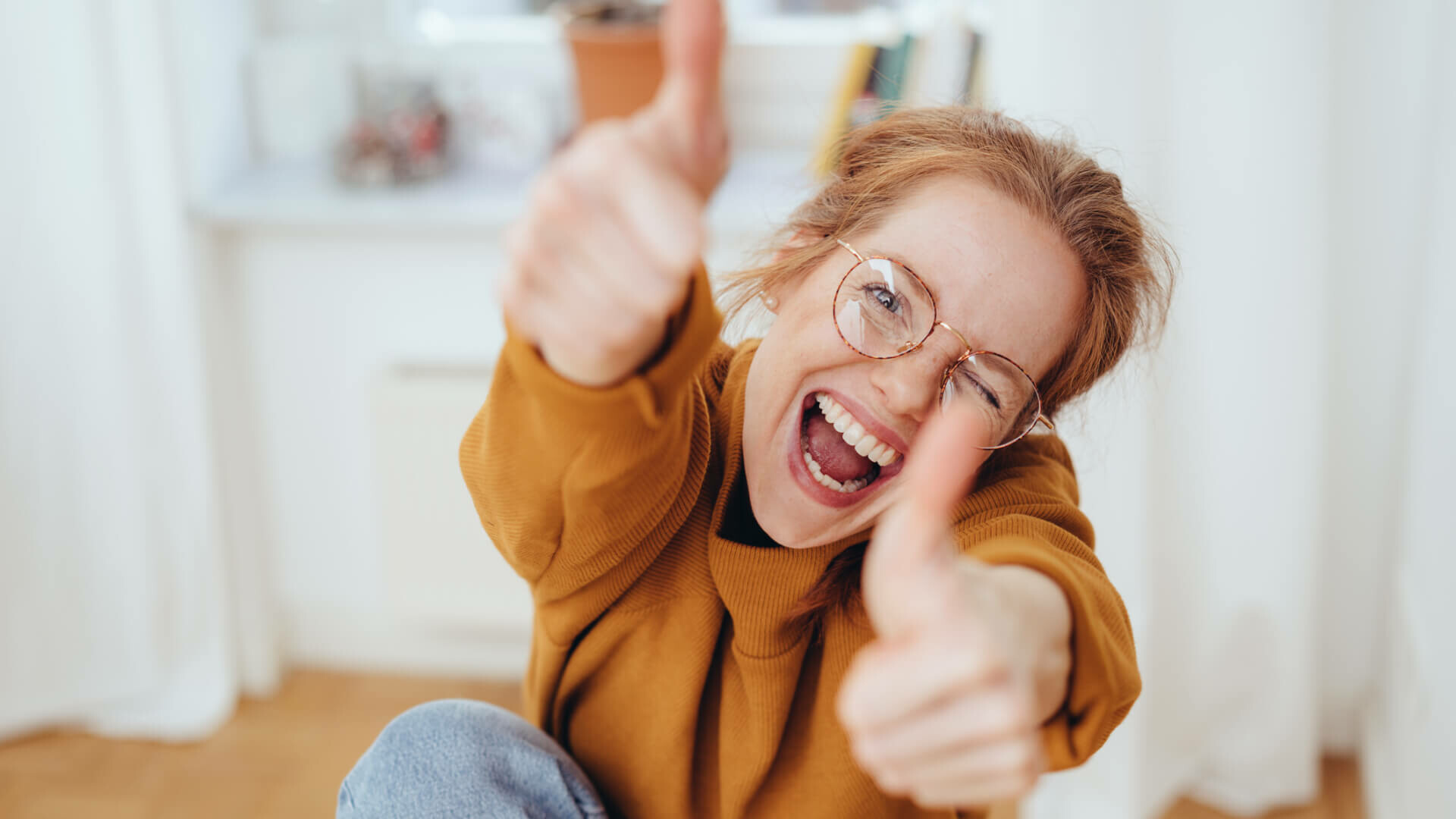 Frau mit Brille, die beide Daumen hoch hält und lacht.