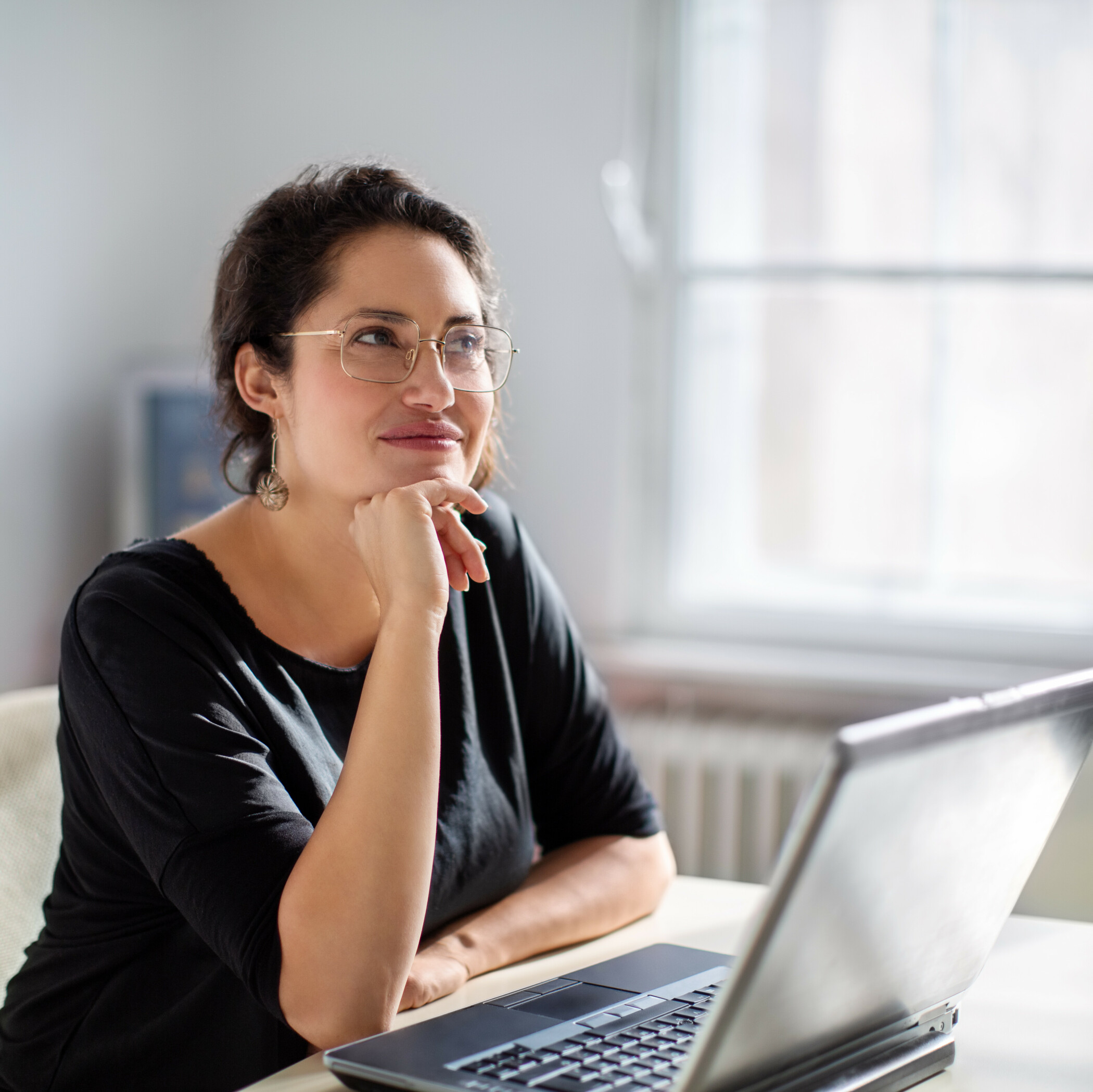 Nachdenkliche Frau sitzt im Büro vor dem Laptop.