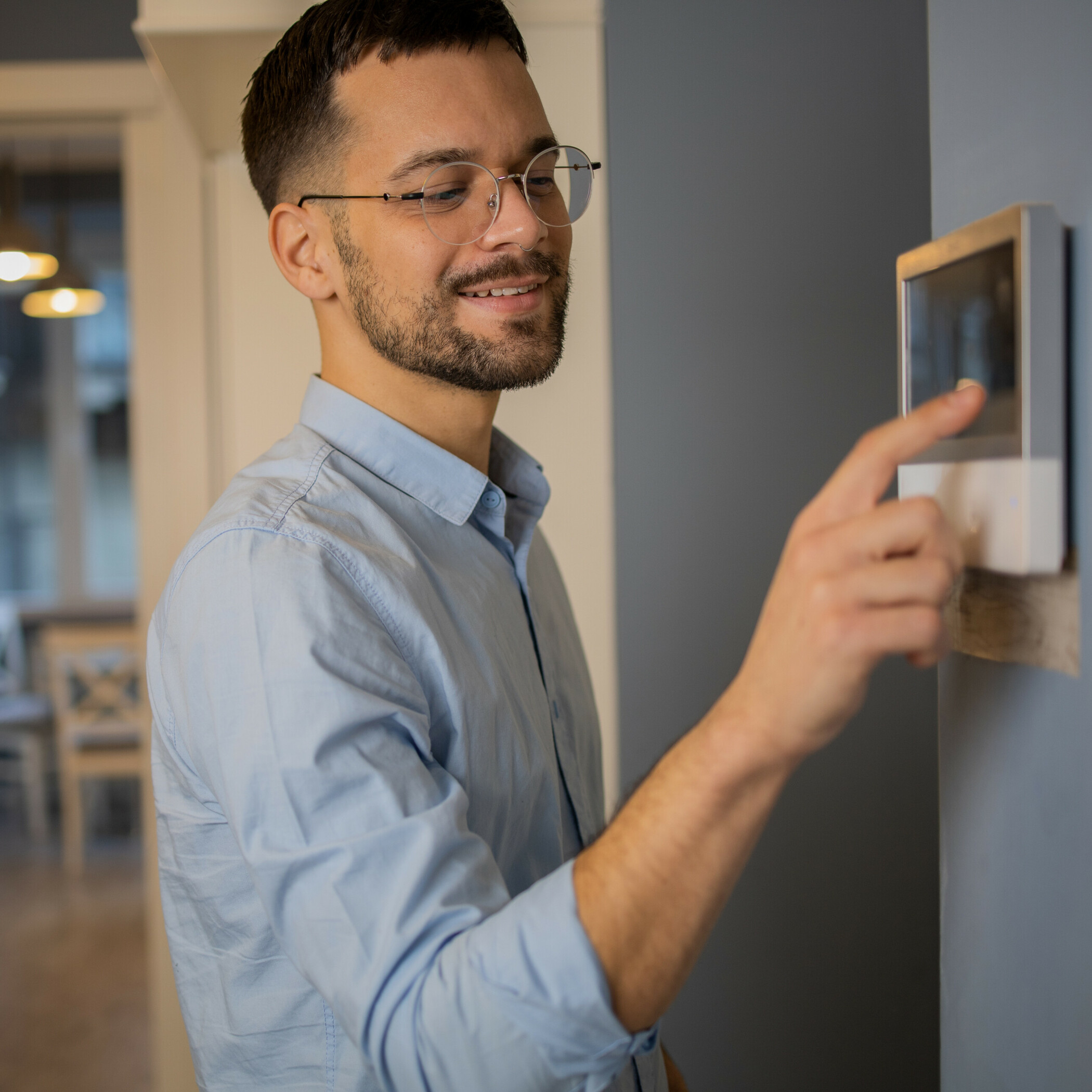 Junger Mann mit blauem Hemd und Brille stellt die Temperatur am Thermostat ein.