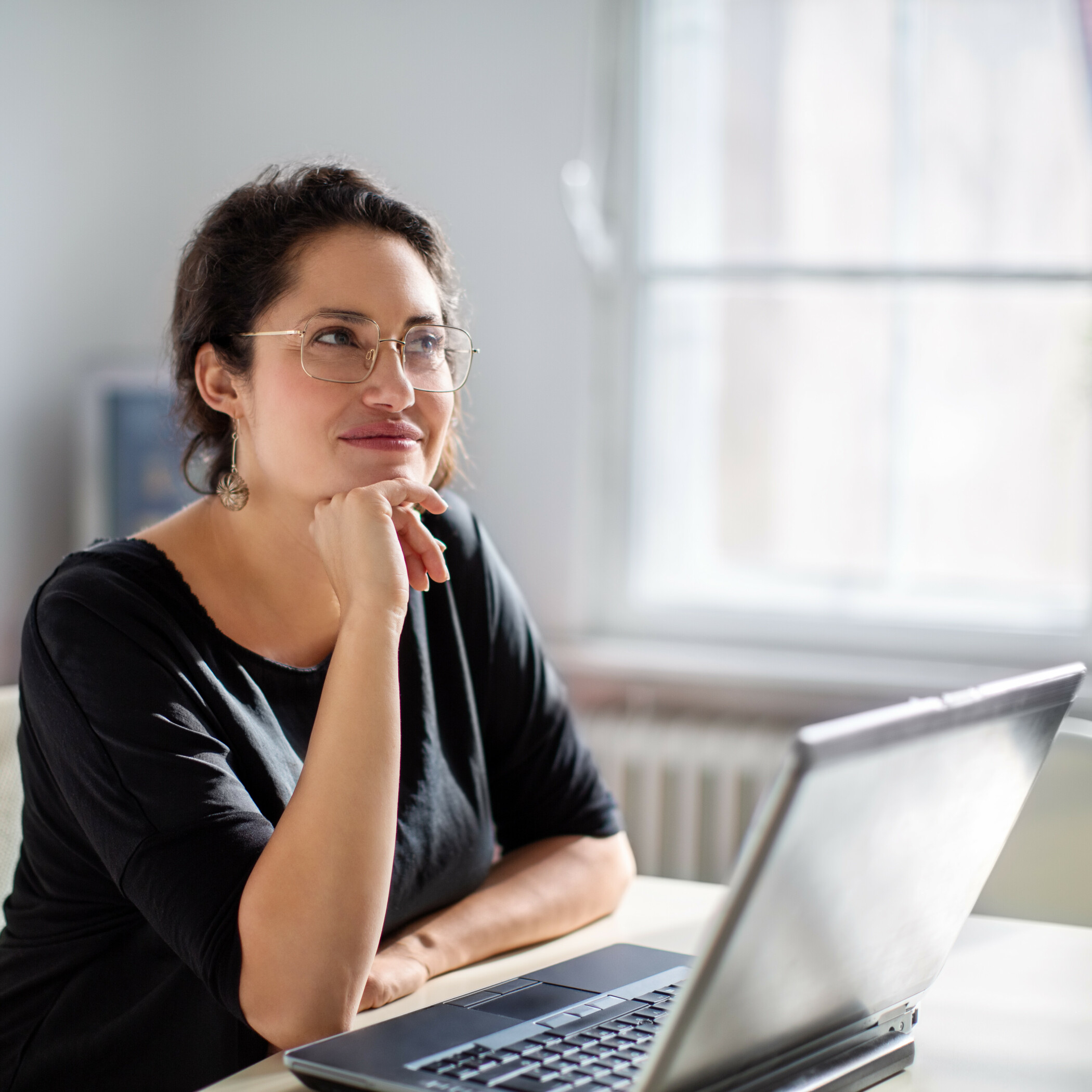 Nachdenkliche Frau sitzt im Büro vor dem Laptop.