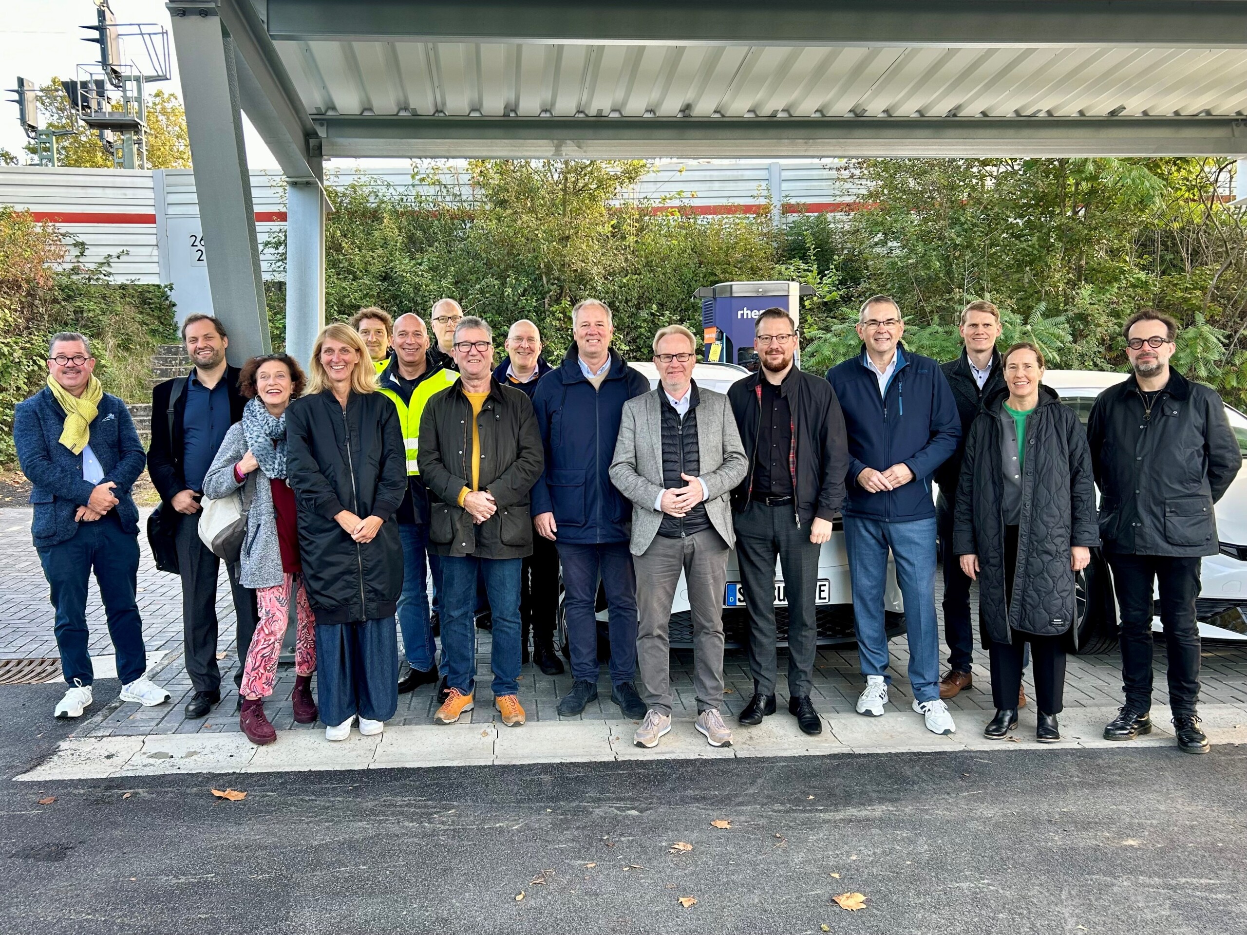 Gruppenfoto der Beteiligten vor einem Ladepark mit Elektrofahrzeugen und rhenag-Ladesäule