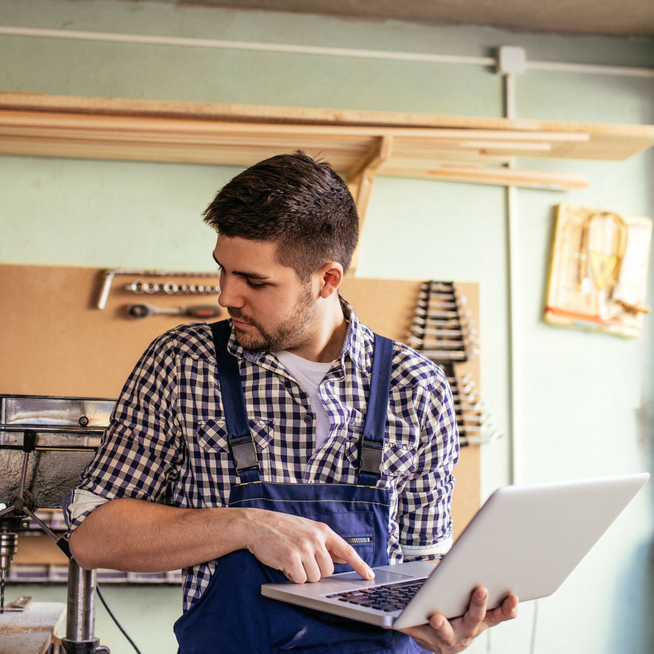 Handwerker mit blauer Latzhose hält und bedient einen Laptop.