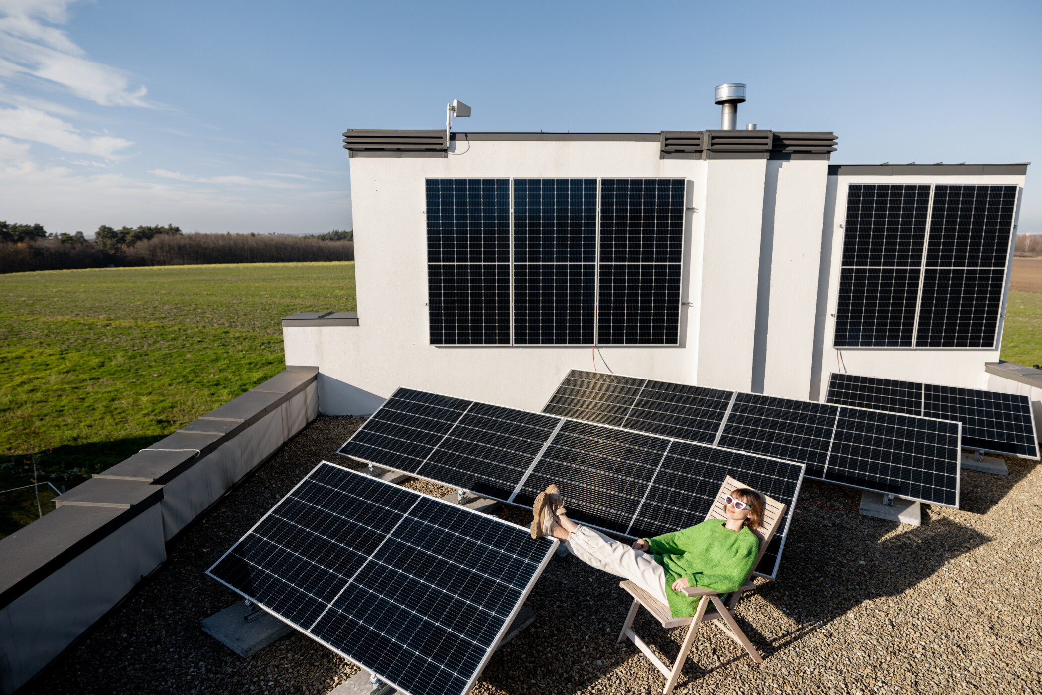 Junge Frau im grünen Pulli sitzt auf dem Hausdach, umgeben von Solarmodulen.