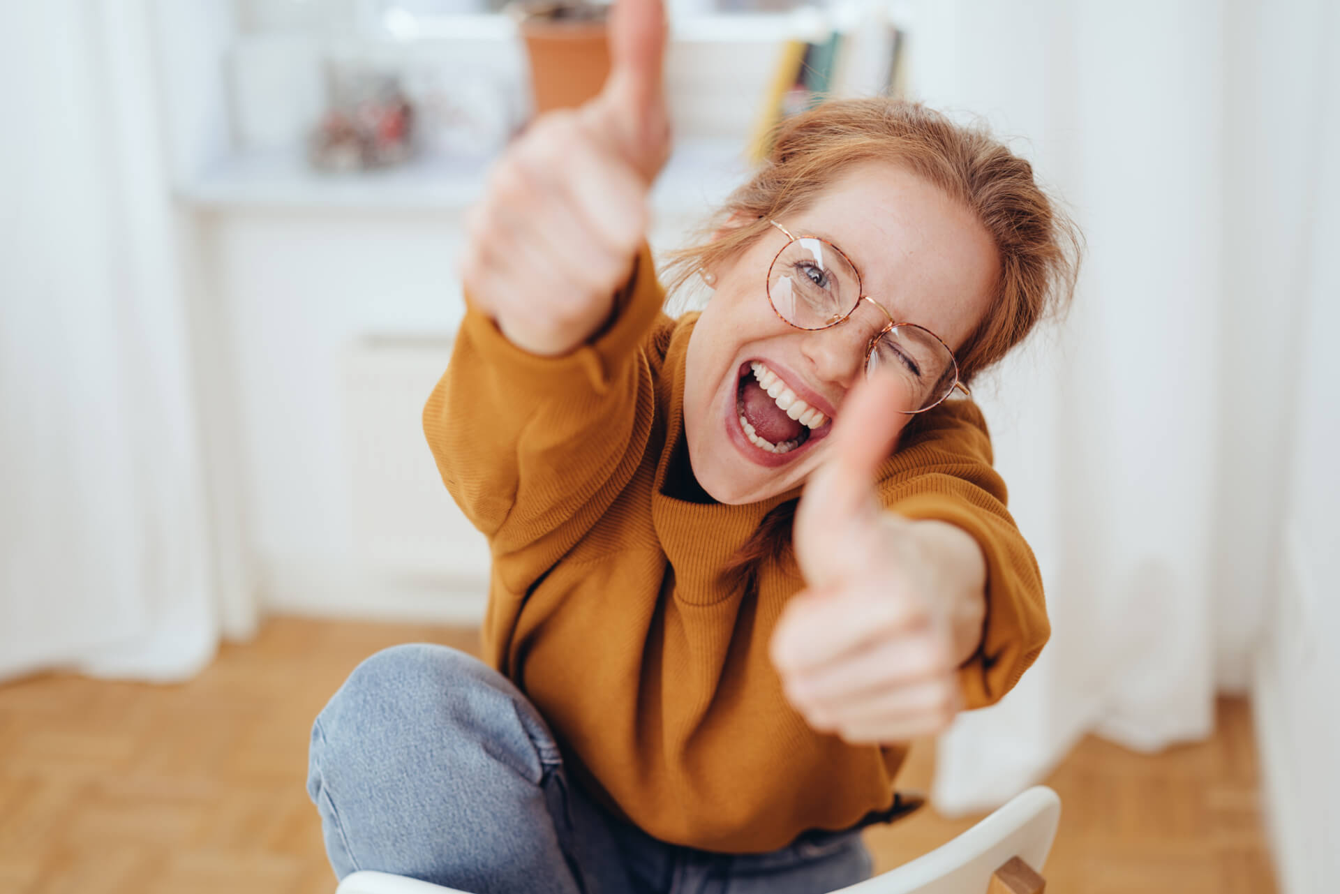 Frau mit Brille, die beide Daumen hoch hält und lacht.