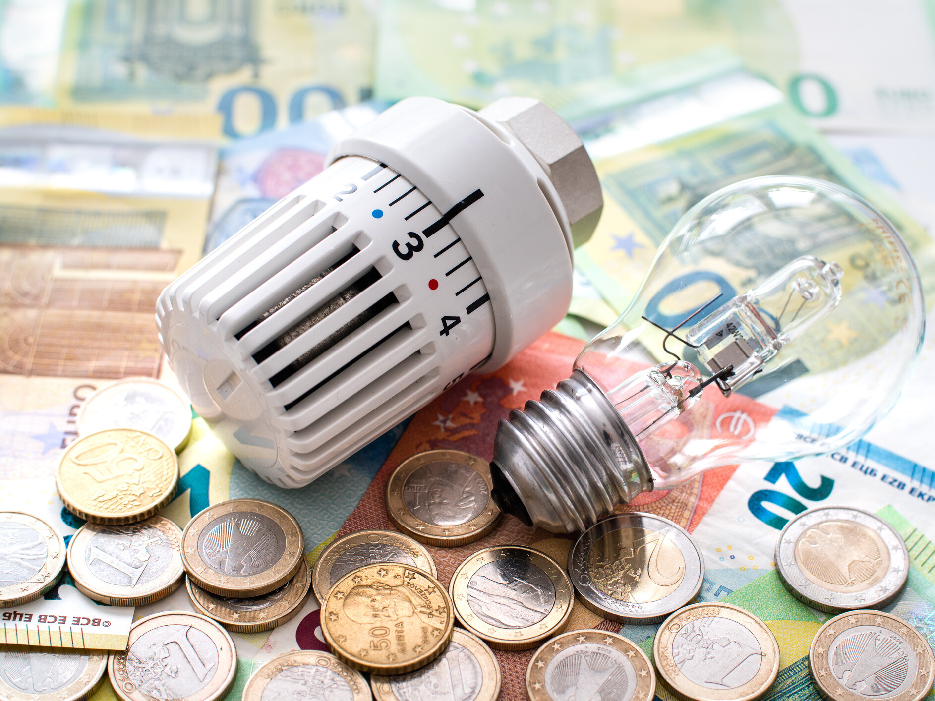 Erfahren Sie, aus welchen Bestandteilen sich der Strompreis zusammensetzt: Glühbirne und Heizungsregler auf Geldscheinen und Münzen
