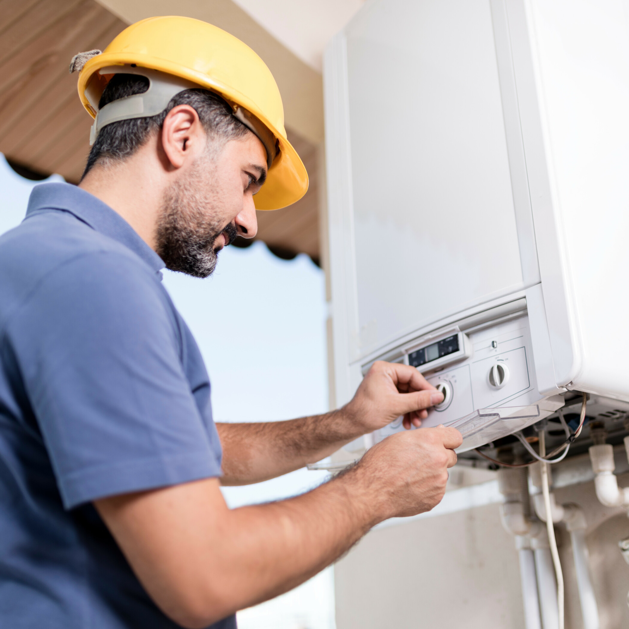 Handwerker mit gelbem Schutzhelm repariert eine Gastherme.