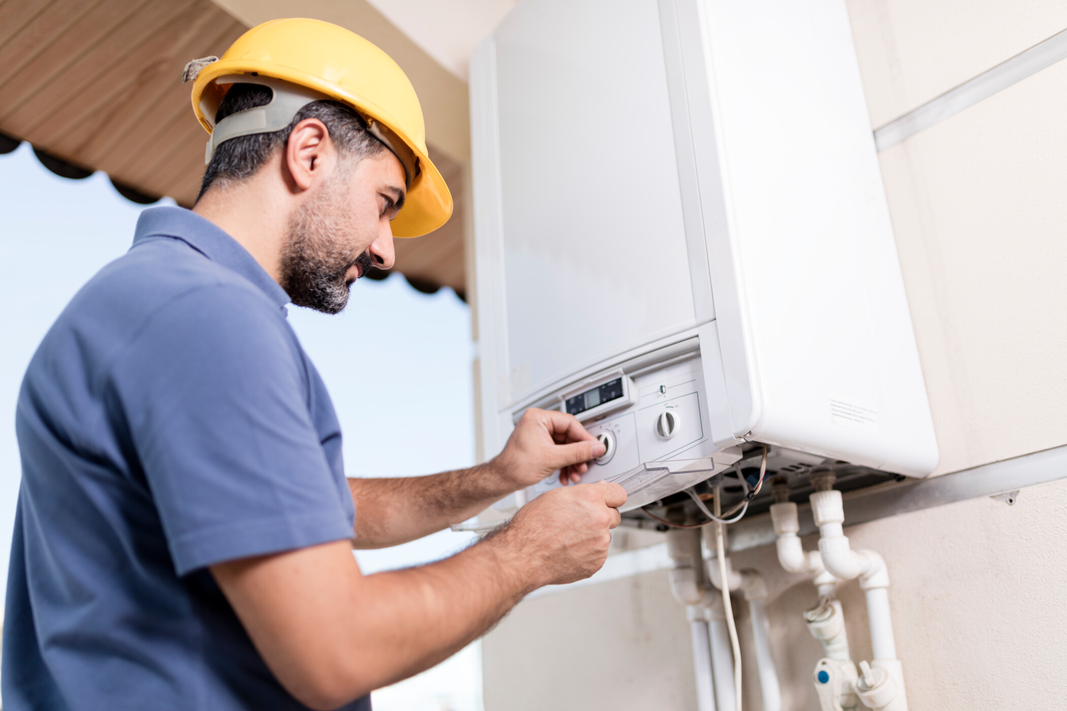 Handwerker mit gelbem Schutzhelm repariert eine Gastherme.