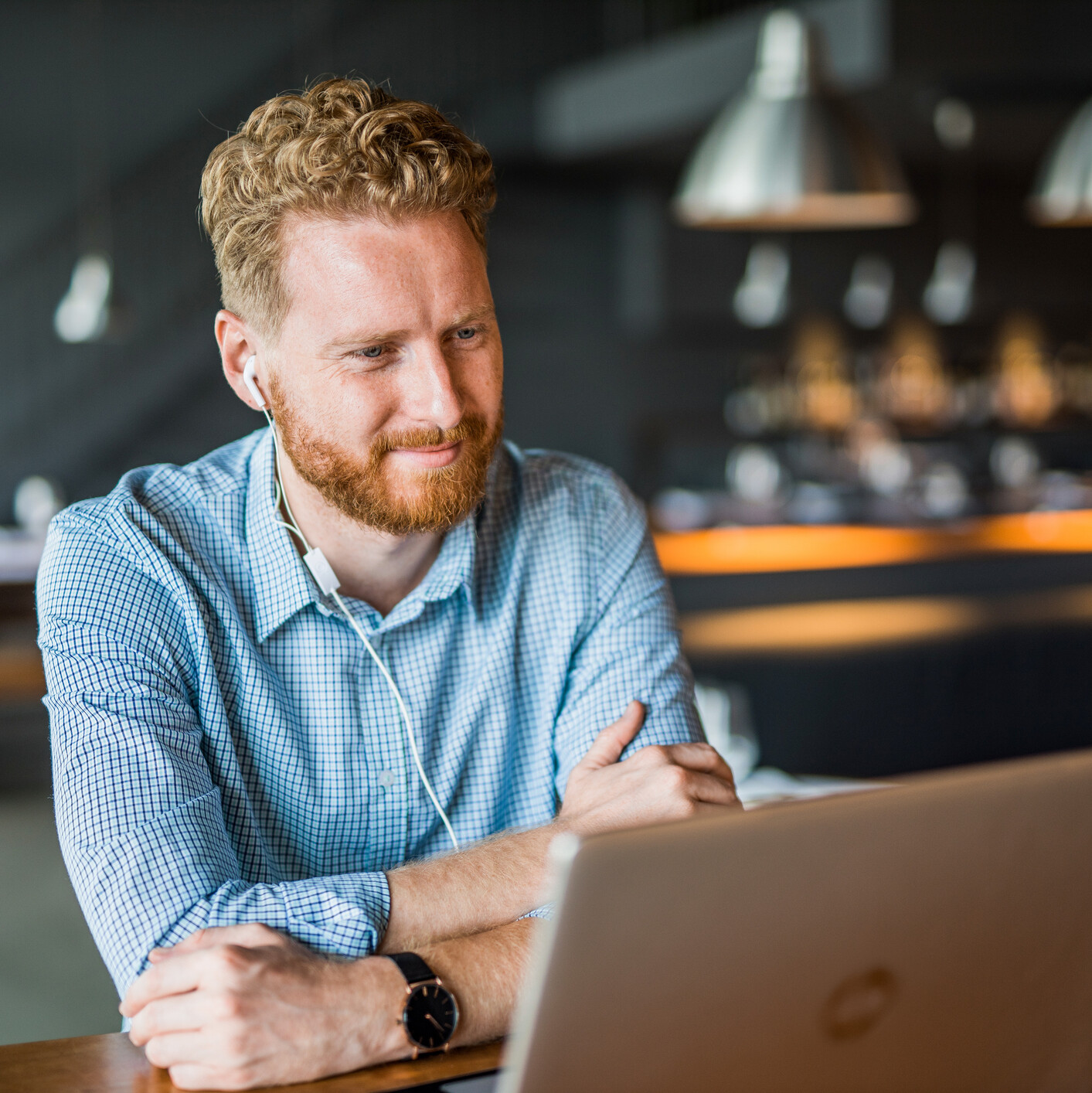 Mann mit blauem Hemd sitzt am Laptop im Wohnzimmer und hat einen Online-Termin.
