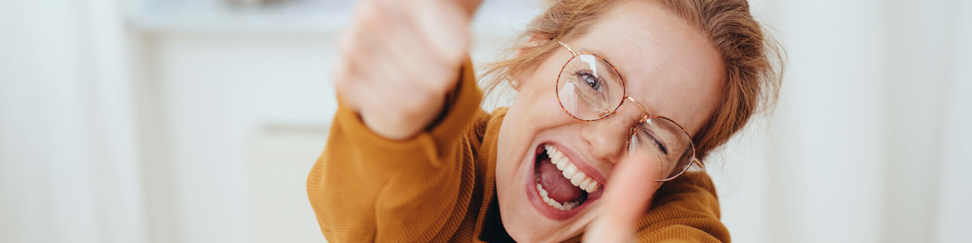 Frau mit Brille, die beide Daumen hoch hält und lacht.