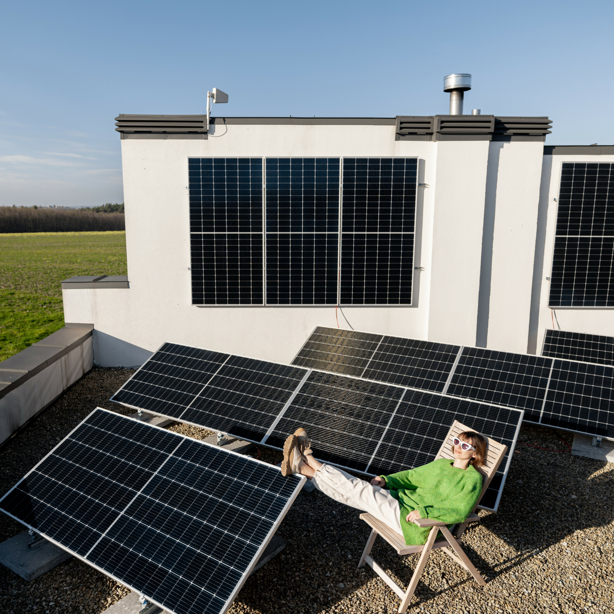 Junge Frau im grünen Pulli sitzt auf dem Hausdach, umgeben von Solarmodulen.