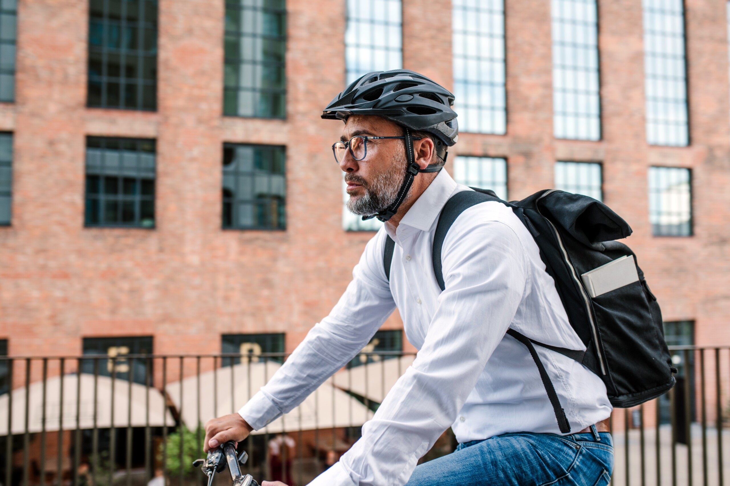 City-Pendler fährt mit dem Fahrrad ins Büro, trägt Rucksack und Helm.